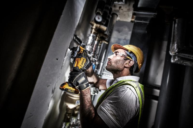 Trabajador usa DEWALT DCS355D2 en una pared, usando equipo de seguridad y guantes.