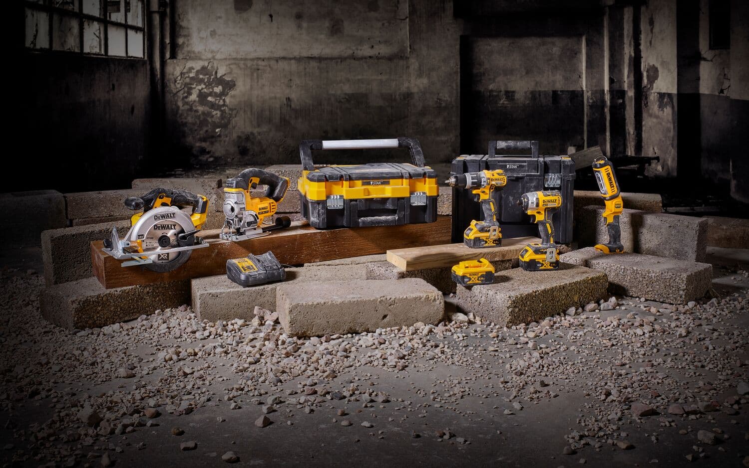 Kit de herramientas DEWALT inalámbricas con caja y baterías sobre bloques en entorno industrial.