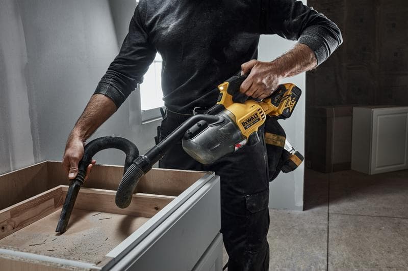 Persona limpia polvo de gabinete de madera usando aspiradora portátil inalámbrica DEWALT en obra.