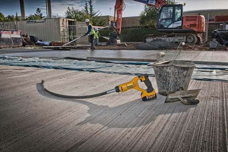 Una herramienta vibradora de hormigón DEWALT DCE531N está situada en una obra, junto a un cubo metálico y una llana sobre