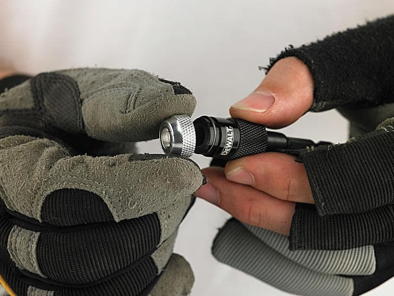 Manos enguantadas ajustan un portabrocas DEWALT.