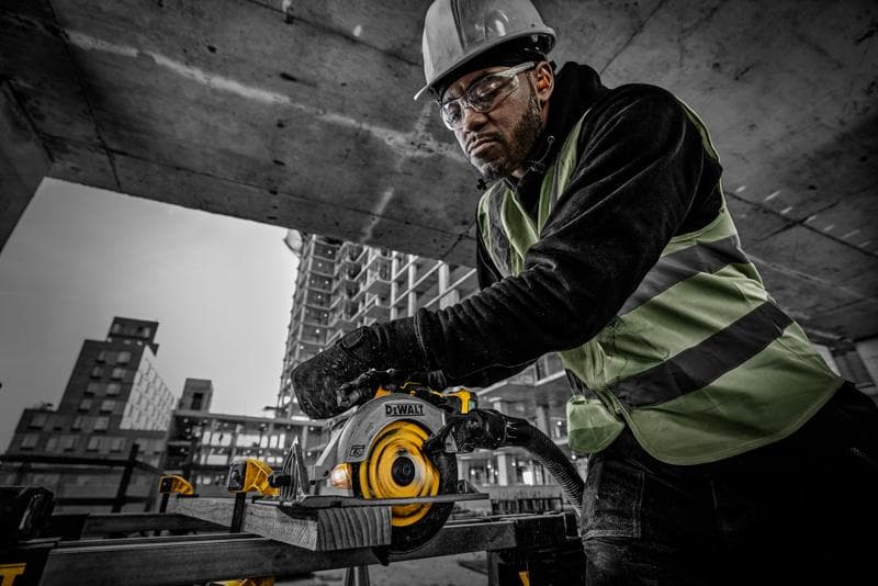 Persona usando sierra circular DEWALT DCS565NT en obra, con ropa de seguridad, cortando madera.