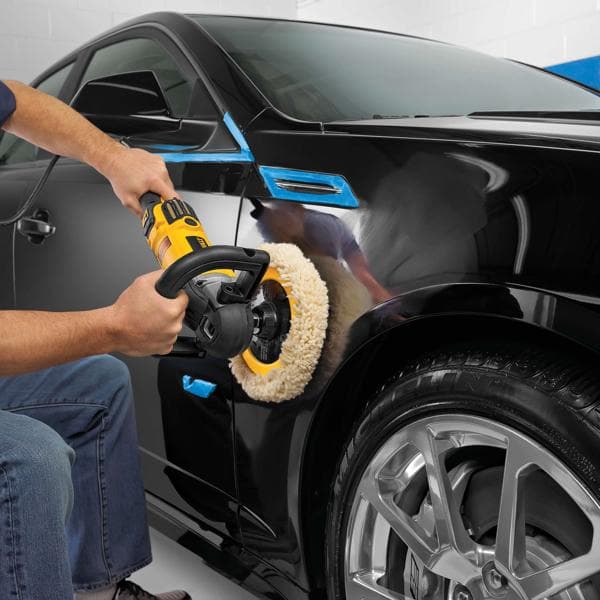 Persona pule el guardabarros de un coche negro con pulidora DEWALT en un garaje.