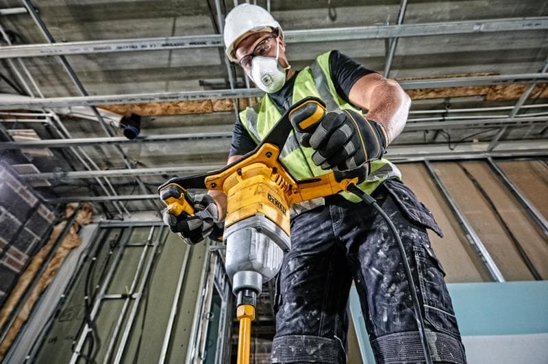 Persona usando mezclador DEWALT DWD241 en obra, vestida con chaleco y guantes de seguridad.
