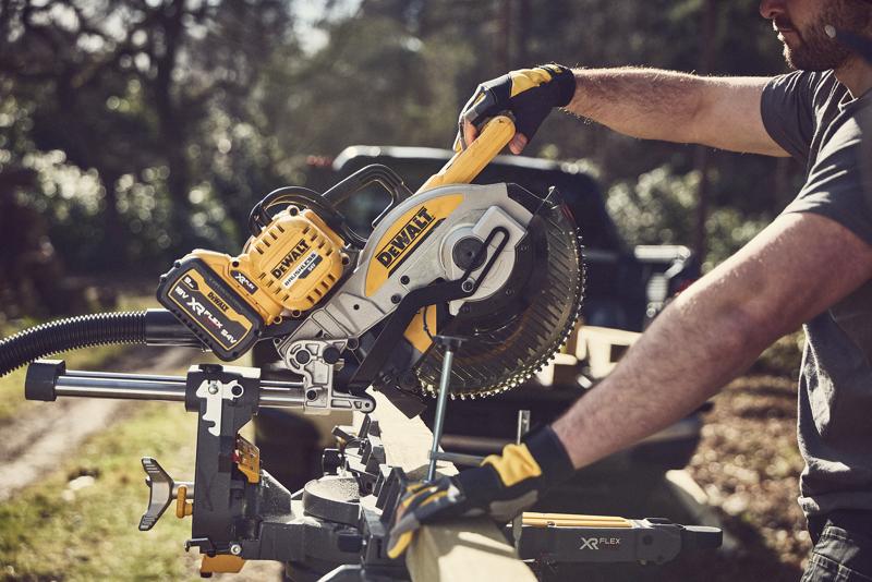 Persona usando una ingletadora DEWALT inalámbrica para cortar madera afuera; herramienta amarillo-negra XR FLEXVOLT.