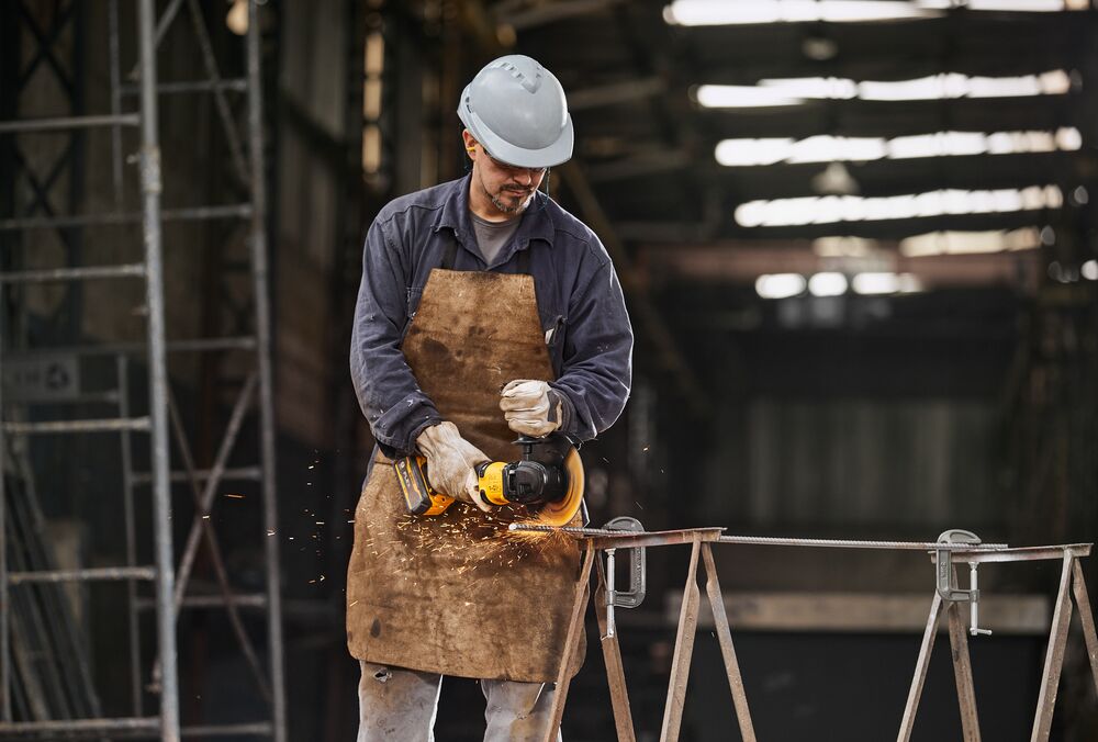 Trabajador usa herramienta DEWALT para cortar metal con equipo de seguridad en ambiente industrial.