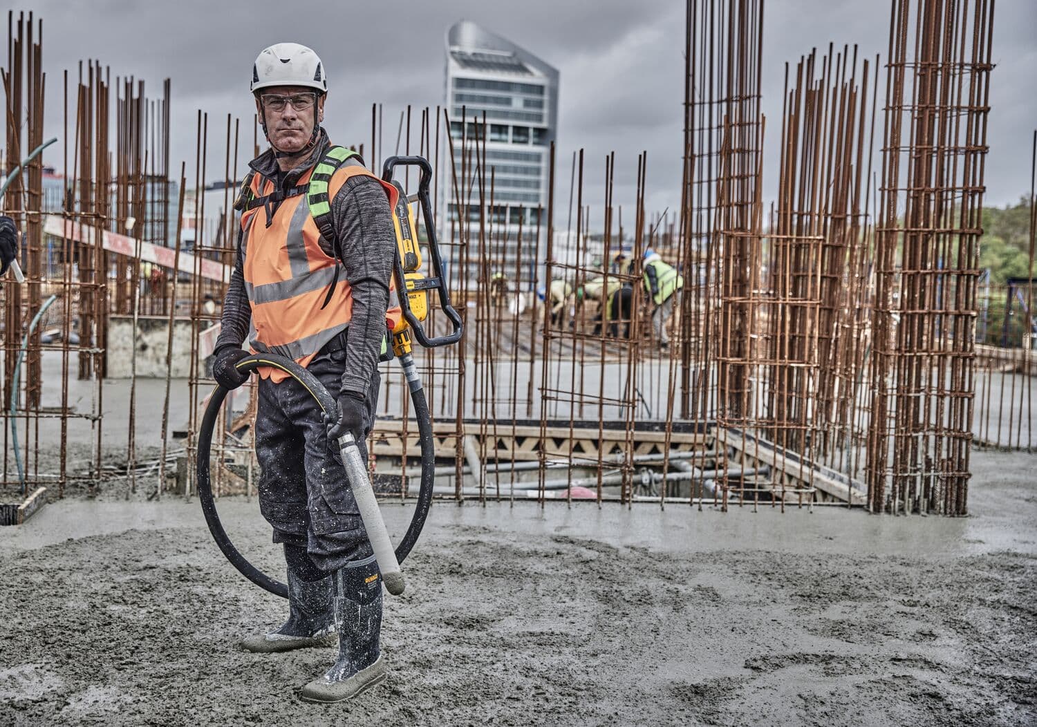 Trabajador usa el vibrador de hormigón DEWALT DCPS310N en obra, rodeado de varillas metálicas y concreto húmedo.