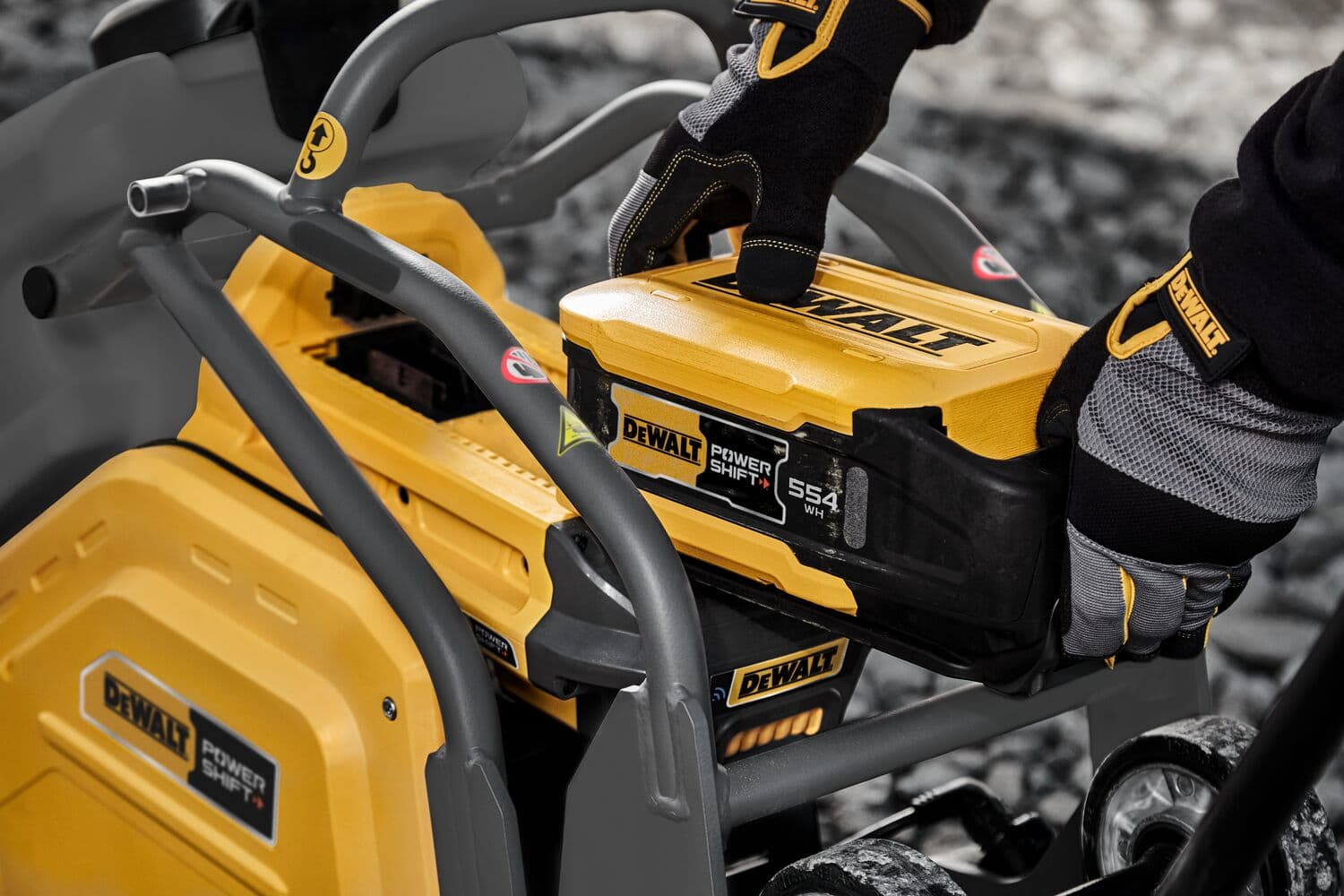 Primer plano de una persona con guantes insertando una batería DEWALT Power Shift en una máquina amarilla DEWALT al aire libre.