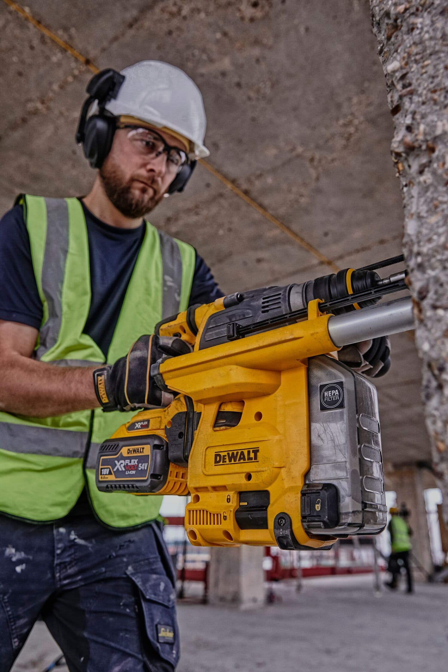 Una persona con equipo de seguridad y chaleco de alta visibilidad sostiene un martillo rotativo inalámbrico DEWALT DCH334X2